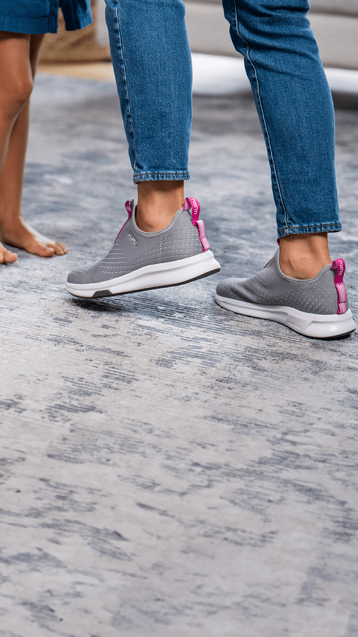 A person with their child, focusing on the feet of each. The mother wears comfortable KURU Footwear shoes on a fluffy rug