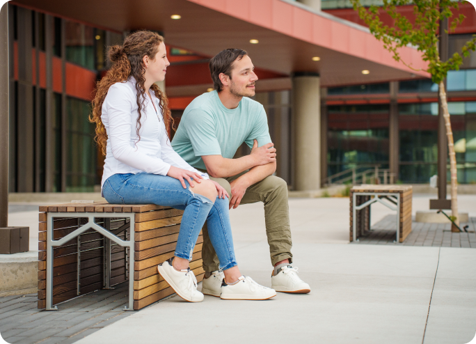 Male and Female sitting on a wooden bench outside of a building