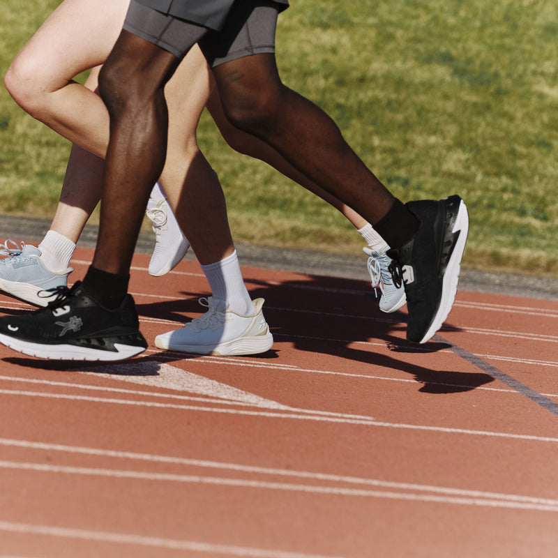 Two runners wearing the KURU ATOM 2 Athletic Sneaker in Gray and Jet Black on a track.
