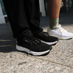 Man wearing KURU ATOM 2 Men's Athletic Sneaker in Jet Black lacing up on stadium bleachers.
