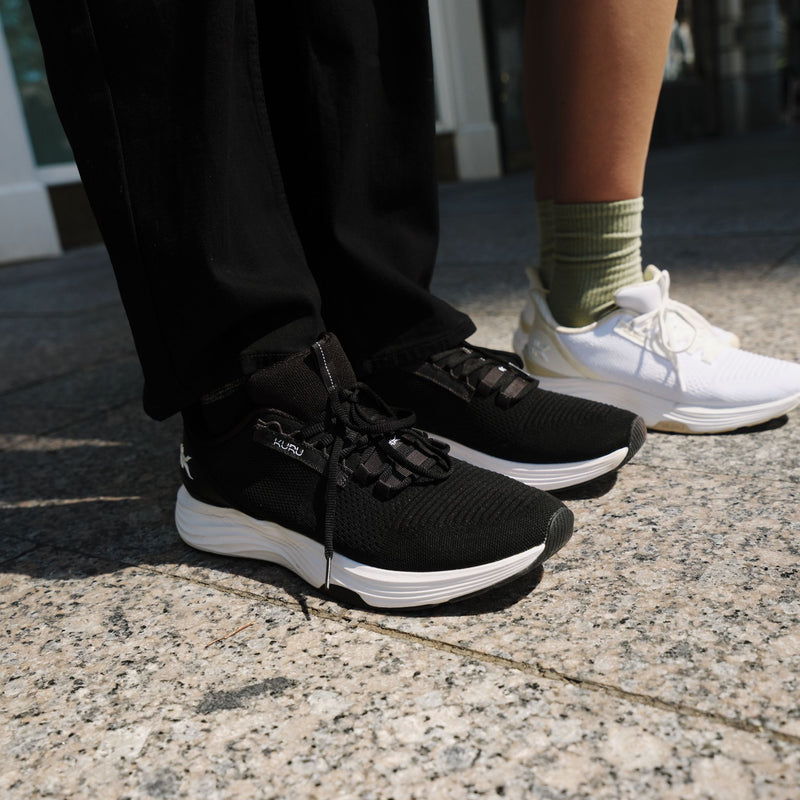 Man wearing KURU ATOM 2 Men's Athletic Sneaker in Jet Black lacing up on stadium bleachers.