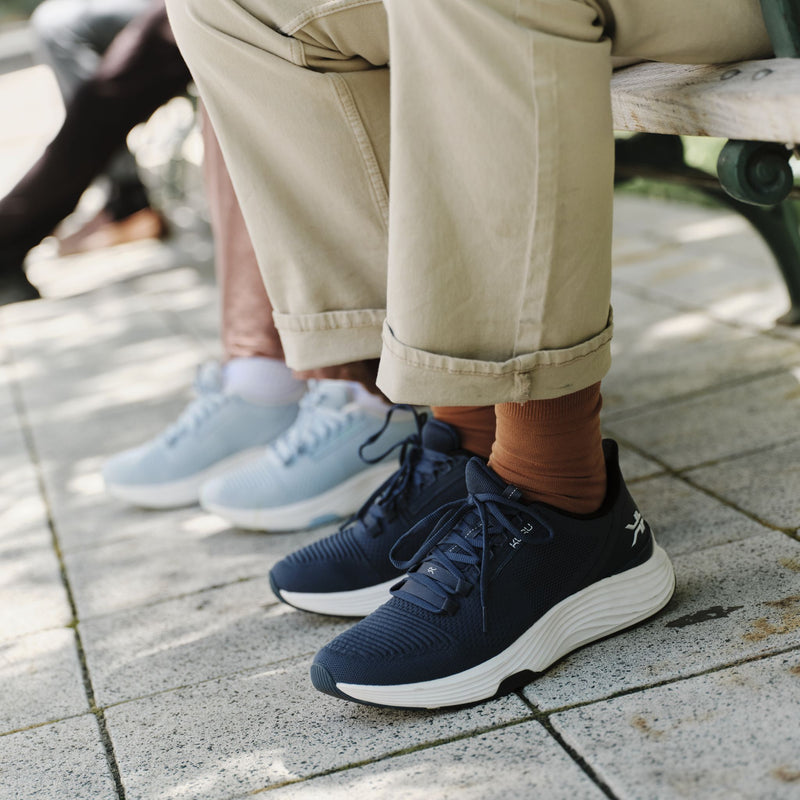 Man wearing KURU ATOM 2 Men's Athletic Sneaker in Night Blue seated on a park bench.