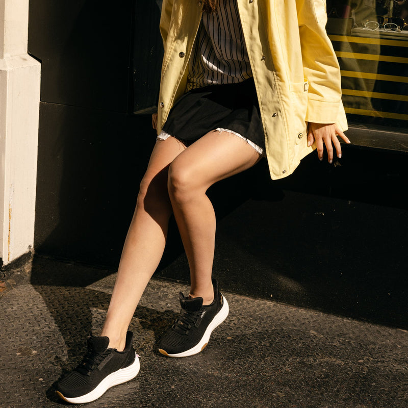 Woman wearing KURU ATOM 2 Women's Athletic Sneaker in Jet Black-Desert Tan relaxing in the city.
