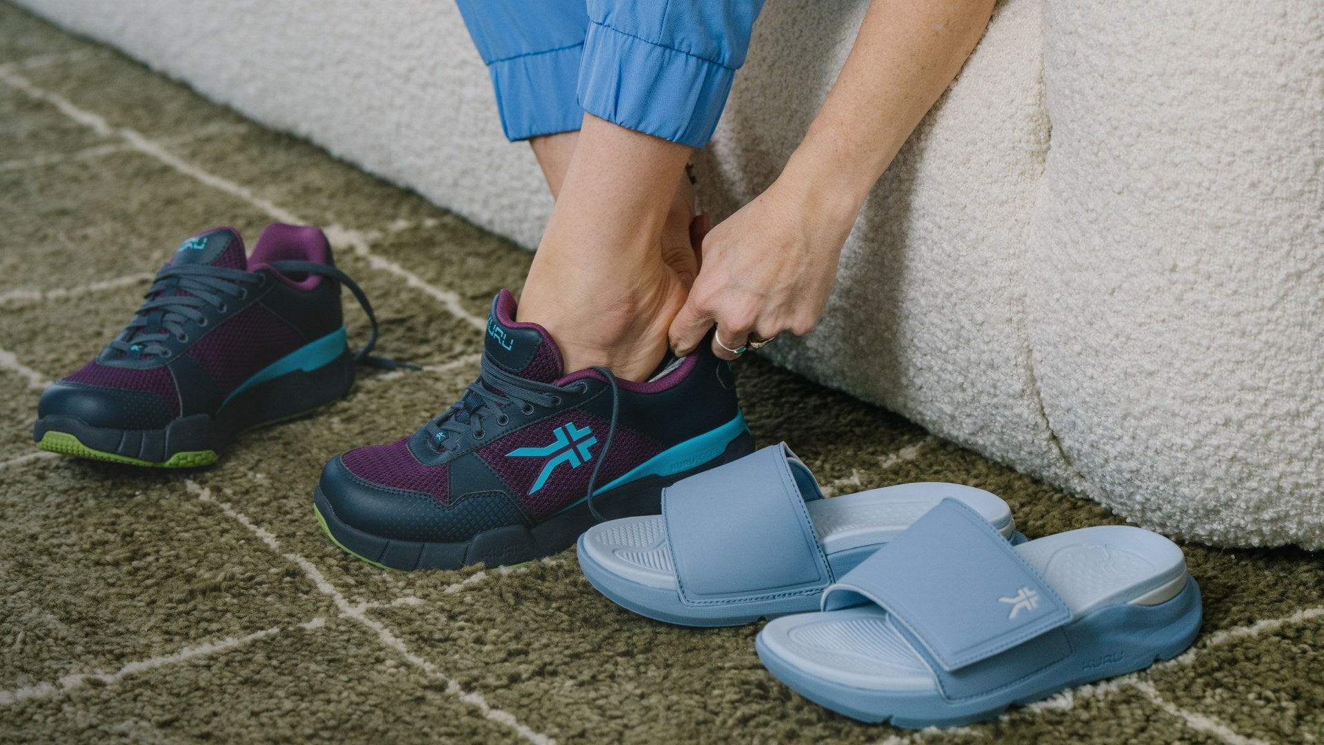Woman putting on KURU QUANTUM 2 sneakers beside KURU slide sandals for all-day relief.