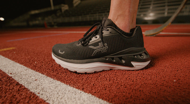 Athlete lacing up KURU shoes trackside at night, close-up lateral view of the KURUSOLE outsole.
