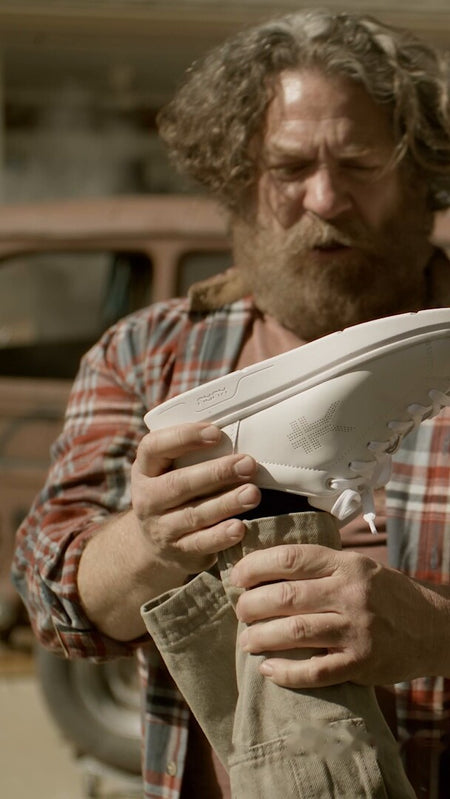 Man holding up white KURU sneakers to show a woman, highlighting relief from all-day foot pain.