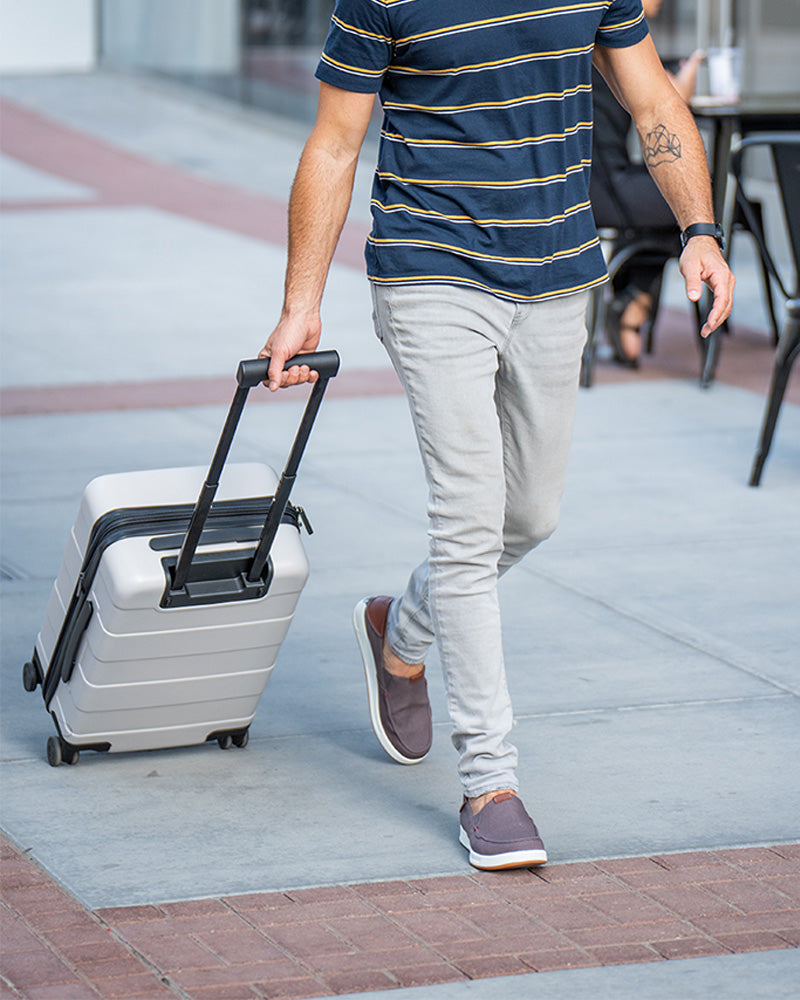Person walking with luggage wearing KURU PACE shoes, ideal for travel and all-day walking comfort.