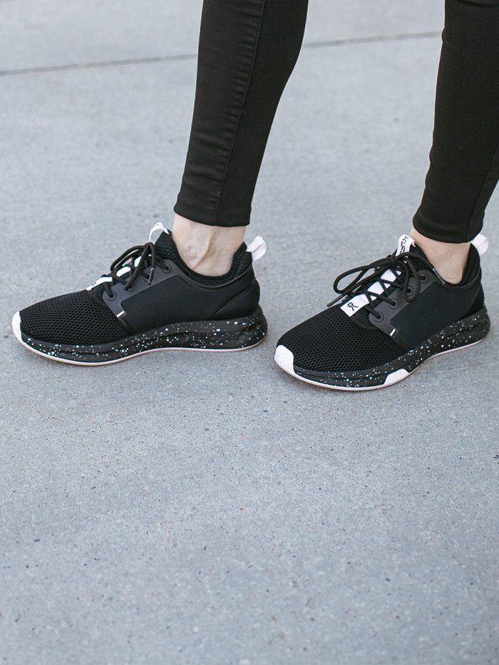close-up of black KURU sneakers with speckled soles worn with black jeans