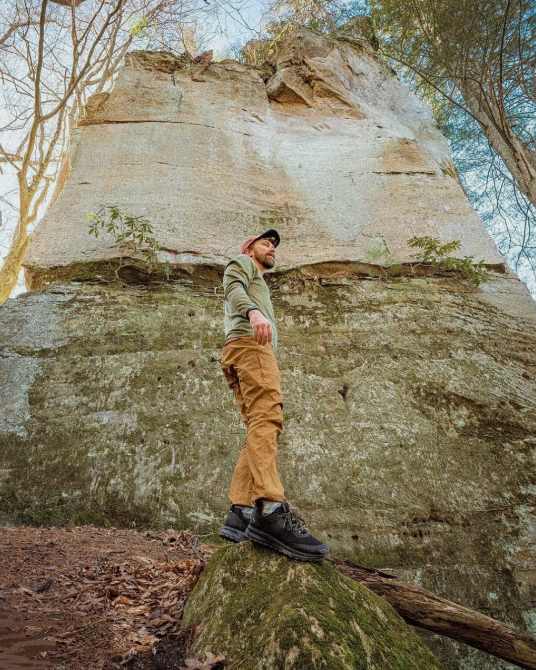 Man standing on a rock in front of a large stone structure with trees in the background