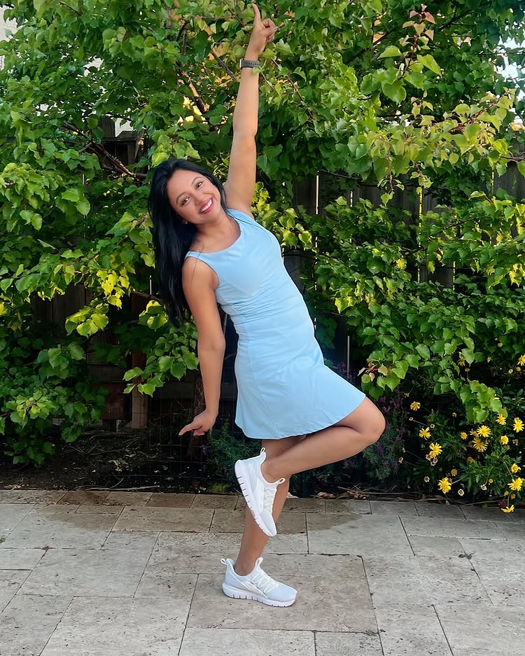 Woman in a light blue dress posing outdoors with greenery in the background